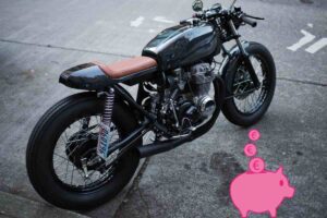 una moto vintage e in basso a destra un salvadanaio con degli euro