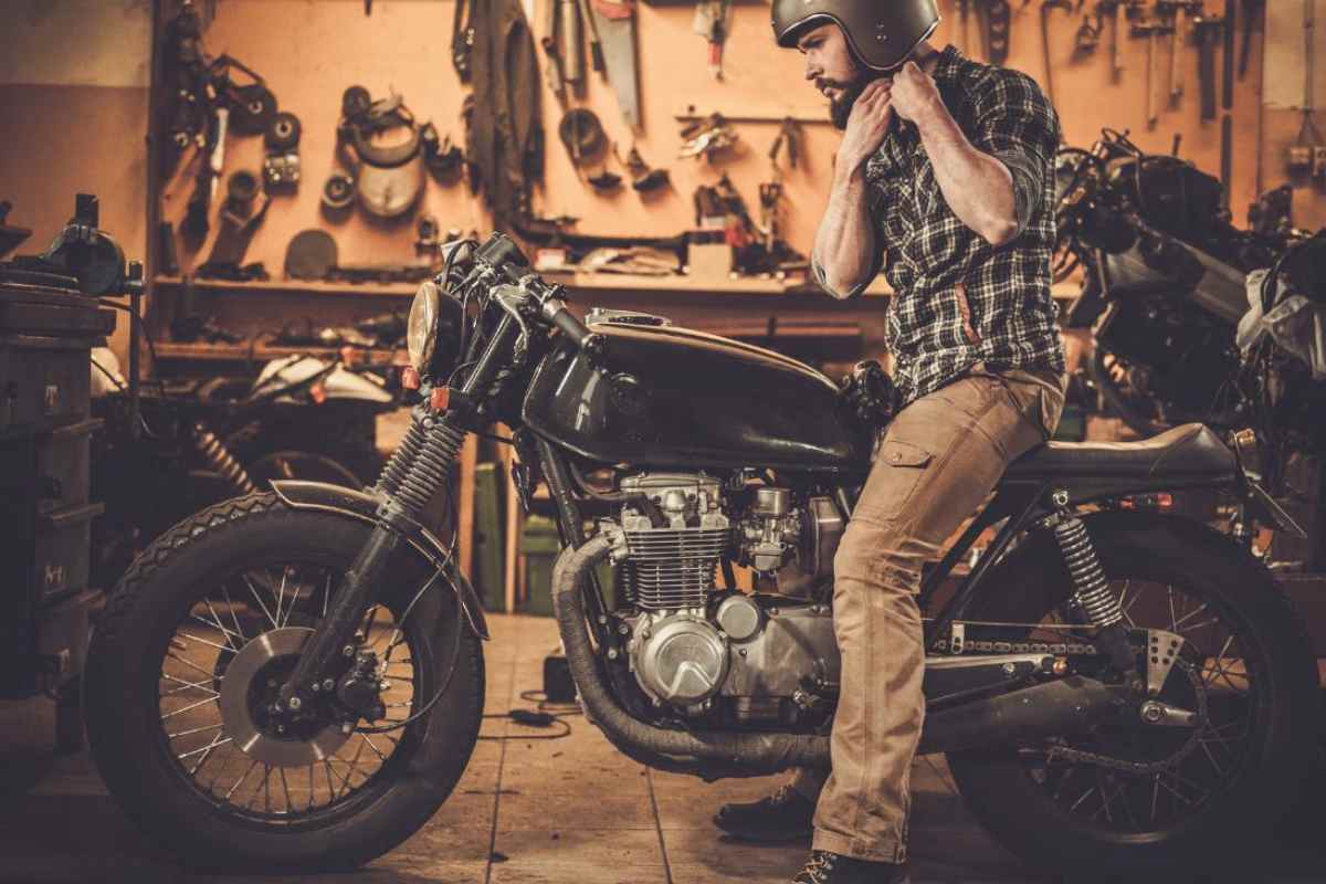 Una moto vintage in officina e in sella un ragazzo che si allaccia il casco