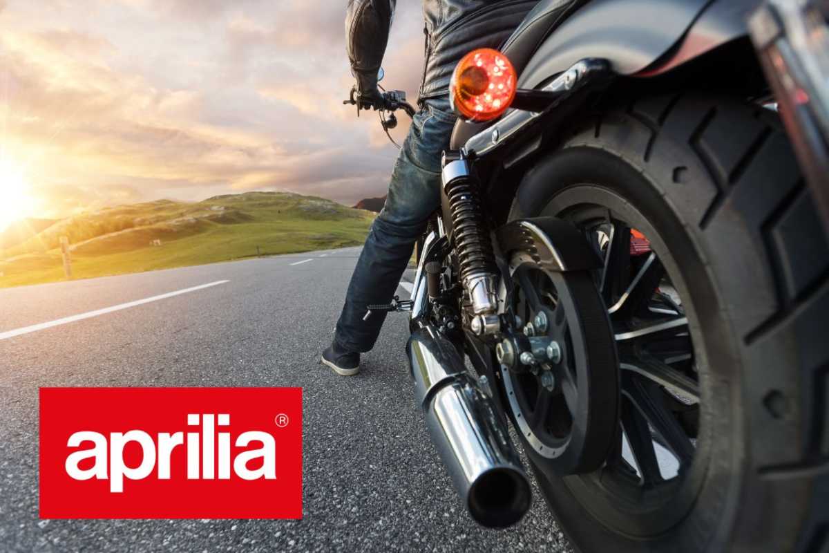 Le ruote di una moto viste da dietro e a sinistra il logo Aprilia